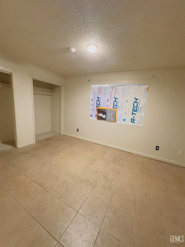 unfurnished bedroom featuring a textured ceiling, light tile patterned floors, baseboards, and two closets