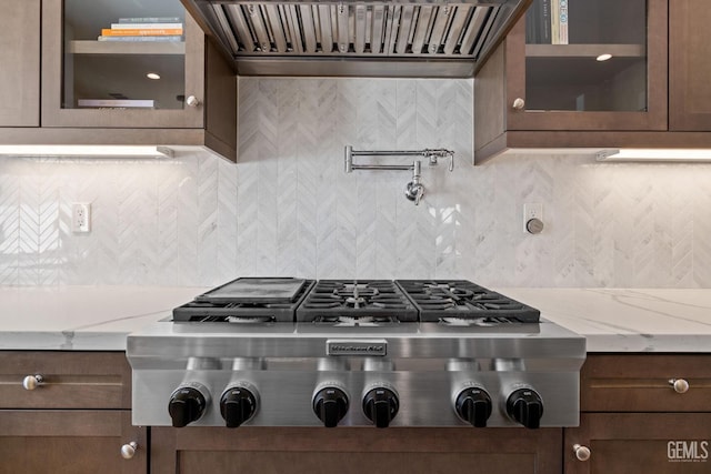 kitchen featuring backsplash, light stone counters, extractor fan, and stainless steel gas cooktop