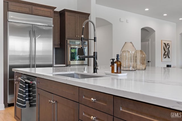 kitchen with dark brown cabinets, light stone counters, sink, and appliances with stainless steel finishes