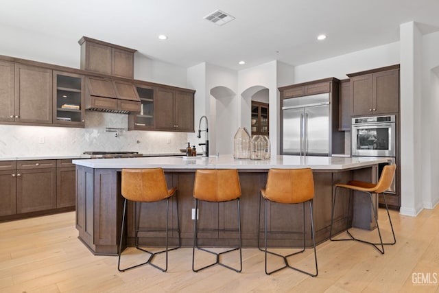 kitchen with stainless steel appliances, light hardwood / wood-style flooring, a center island with sink, and a breakfast bar area