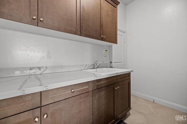 kitchen featuring light stone countertops, dark brown cabinetry, and sink