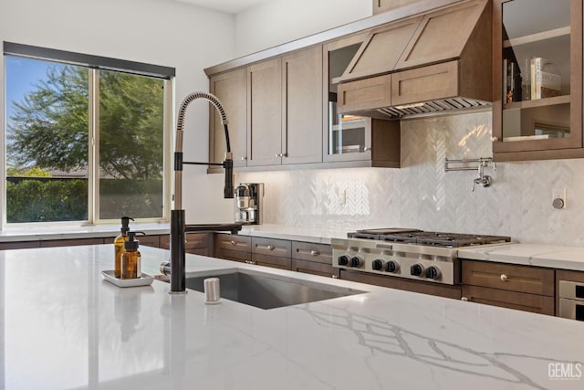 kitchen with stainless steel gas stovetop, custom exhaust hood, sink, light stone countertops, and tasteful backsplash