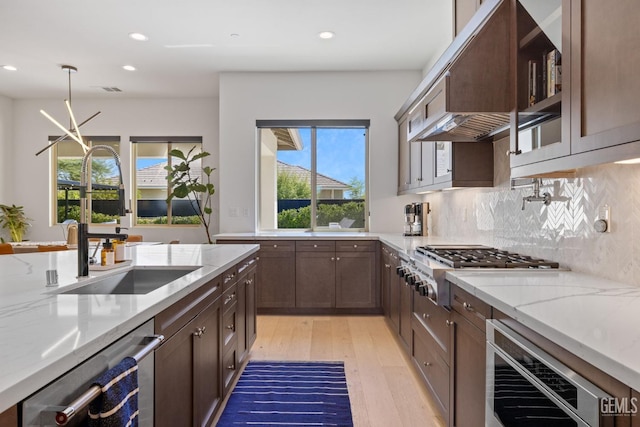 kitchen featuring light stone countertops, appliances with stainless steel finishes, custom range hood, beverage cooler, and decorative light fixtures