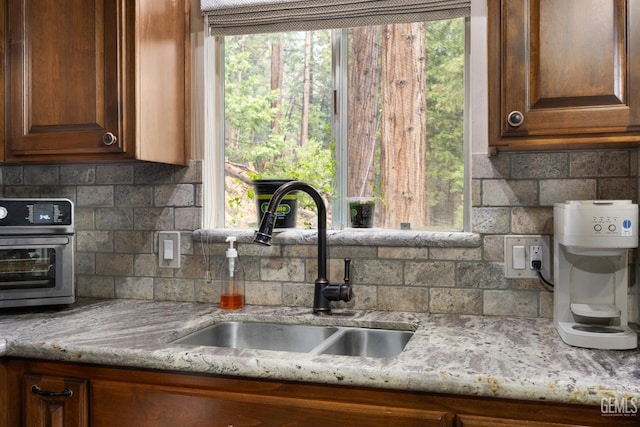 kitchen with tasteful backsplash, plenty of natural light, sink, and light stone counters