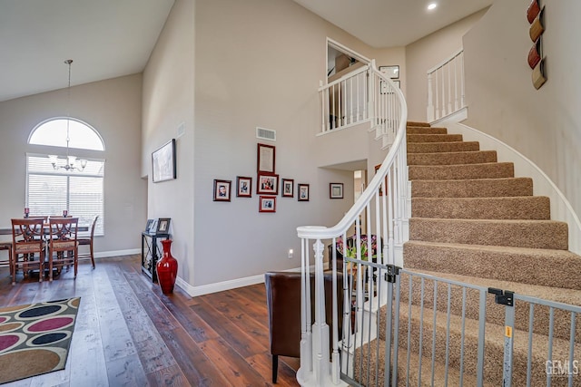 stairway with a towering ceiling, an inviting chandelier, and hardwood / wood-style flooring