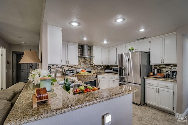 kitchen with kitchen peninsula, appliances with stainless steel finishes, white cabinetry, and wall chimney range hood