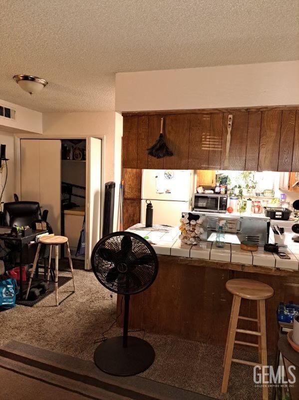 kitchen with tile counters, white refrigerator, carpet floors, and a textured ceiling