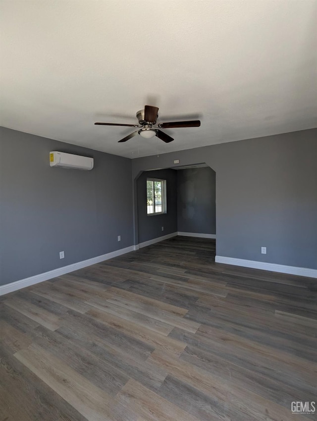 spare room featuring a wall mounted AC, a ceiling fan, baseboards, and dark wood-style flooring