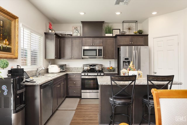 kitchen with hardwood / wood-style floors, a center island, a kitchen breakfast bar, sink, and appliances with stainless steel finishes