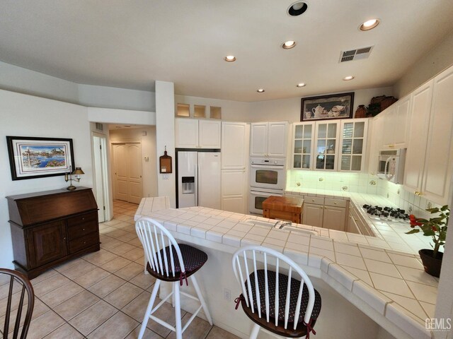 8707 Beau Maison Way, Bakersfield, CA 93311 - kitchen featuring white appliances, tile countertops, a peninsula, glass insert cabinets, and a breakfast bar area