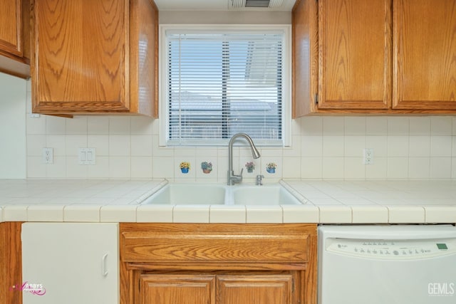 kitchen featuring decorative backsplash, brown cabinets, dishwasher, and a sink