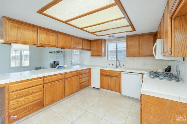 kitchen with decorative backsplash, brown cabinetry, light tile patterned flooring, a sink, and white appliances