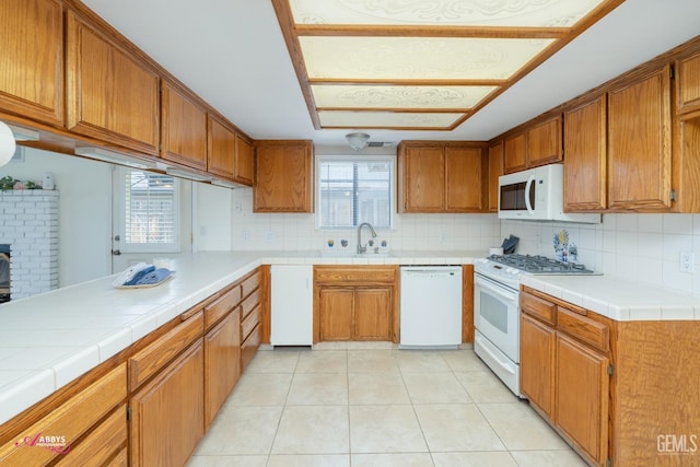 kitchen with white appliances, light tile patterned floors, brown cabinetry, and a sink