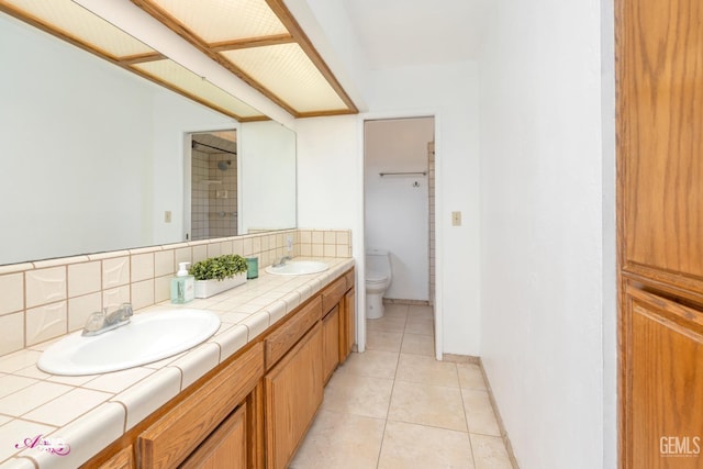 bathroom featuring tile patterned flooring, toilet, a sink, backsplash, and double vanity