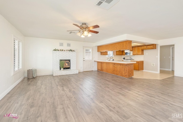 kitchen featuring white microwave, a peninsula, visible vents, open floor plan, and brown cabinetry