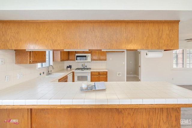 kitchen featuring brown cabinets, light countertops, a sink, white appliances, and a peninsula