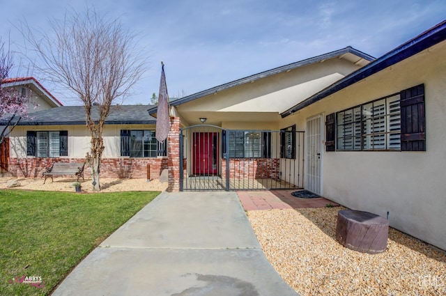 view of front facade with brick siding, a front yard, a gate, and stucco siding