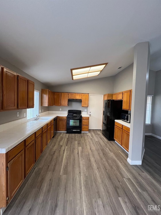 kitchen featuring sink, range hood, wood-type flooring, black appliances, and vaulted ceiling