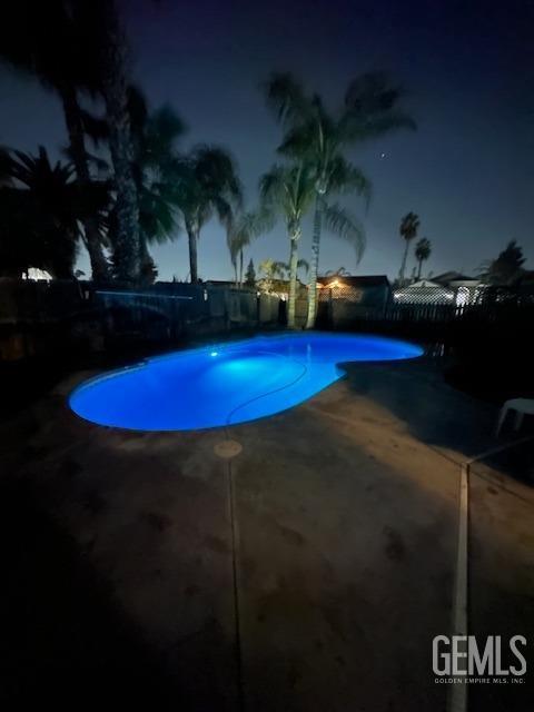 pool at night featuring a patio area