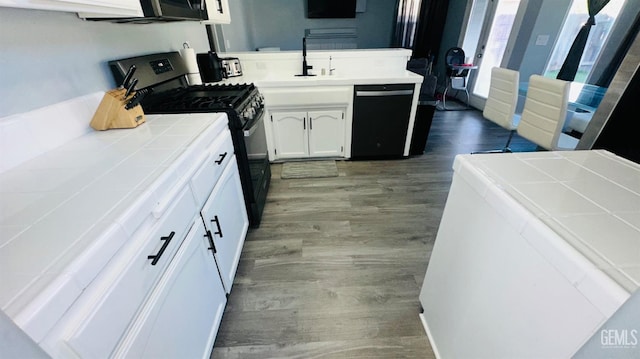 kitchen with tile countertops, dishwasher, hardwood / wood-style floors, white cabinets, and gas range