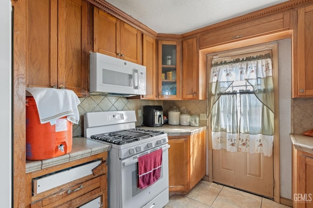 kitchen featuring decorative backsplash, light tile patterned floors, white appliances, and tile countertops