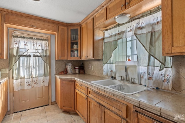 kitchen with tile countertops, backsplash, sink, light tile patterned floors, and a textured ceiling