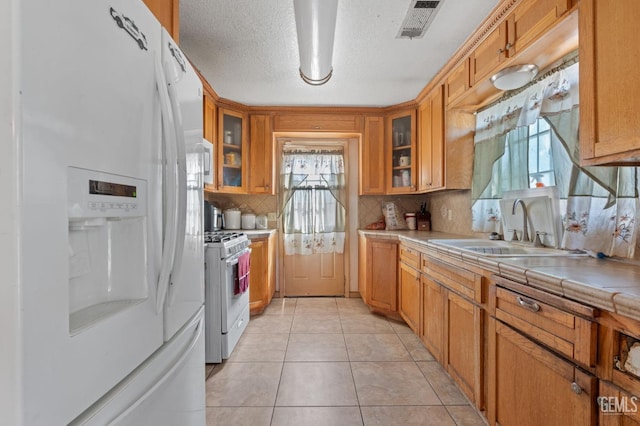 kitchen with tile counters, sink, a textured ceiling, white appliances, and light tile patterned floors