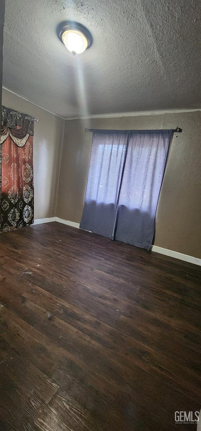 empty room with wood finished floors, a textured ceiling, and baseboards