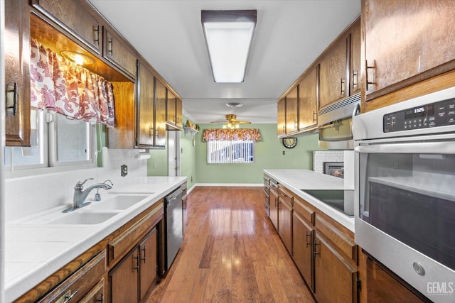 kitchen with stainless steel appliances, ceiling fan, sink, tile countertops, and hardwood / wood-style floors