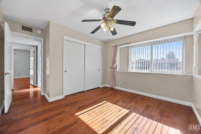 unfurnished bedroom with a textured ceiling, ceiling fan, dark wood-type flooring, and a closet