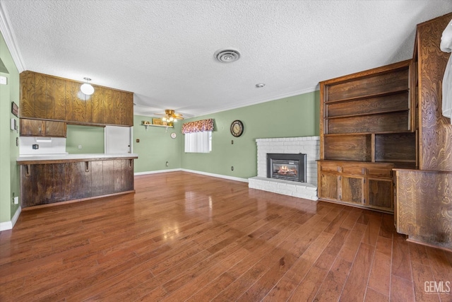 unfurnished living room featuring ceiling fan, a brick fireplace, dark hardwood / wood-style flooring, a textured ceiling, and ornamental molding