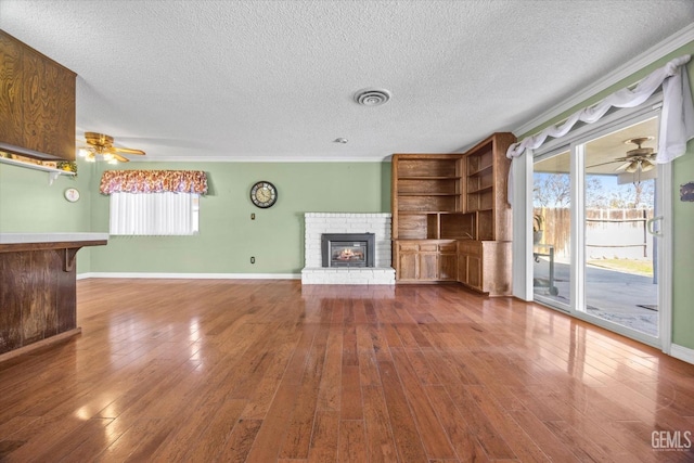 unfurnished living room with hardwood / wood-style floors, a textured ceiling, and a brick fireplace