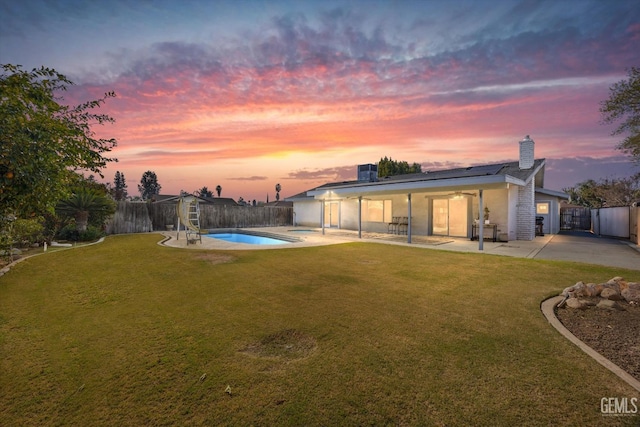 back house at dusk featuring a fenced in pool, a yard, and a patio