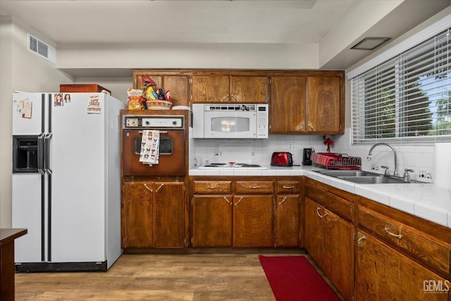 808 La Puente Dr, Bakersfield, CA 93309 - kitchen with white appliances, a sink, light wood-style flooring, decorative backsplash, and tile counters