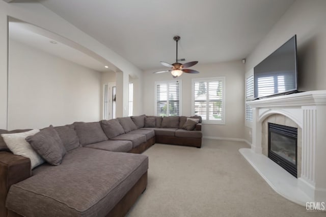 living area with a tile fireplace, baseboards, a ceiling fan, and light colored carpet