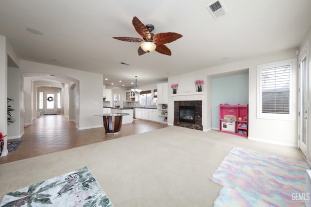 living area with visible vents, ceiling fan with notable chandelier, arched walkways, and light colored carpet