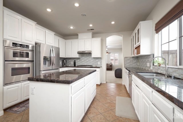 kitchen with arched walkways, stainless steel appliances, a sink, white cabinetry, and a center island