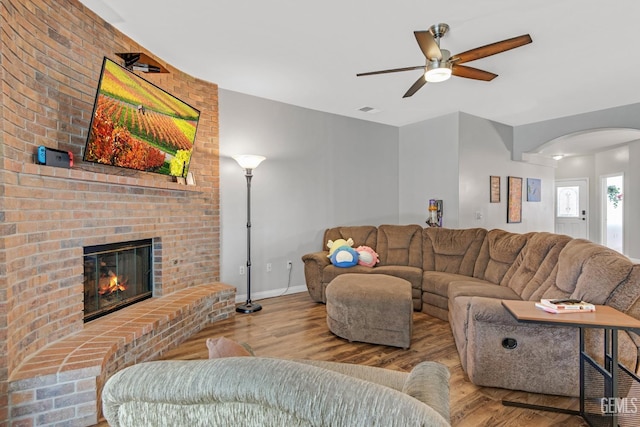 living area featuring a brick fireplace, light wood-style flooring, arched walkways, and baseboards