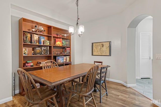 dining space with arched walkways, a notable chandelier, baseboards, and wood finished floors