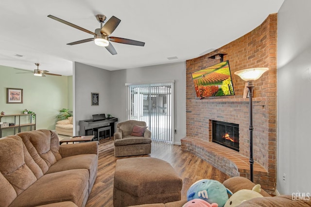 living area featuring light wood-style floors, a fireplace, and a ceiling fan