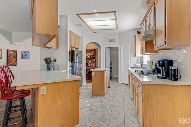 kitchen featuring light countertops, under cabinet range hood, and a breakfast bar area