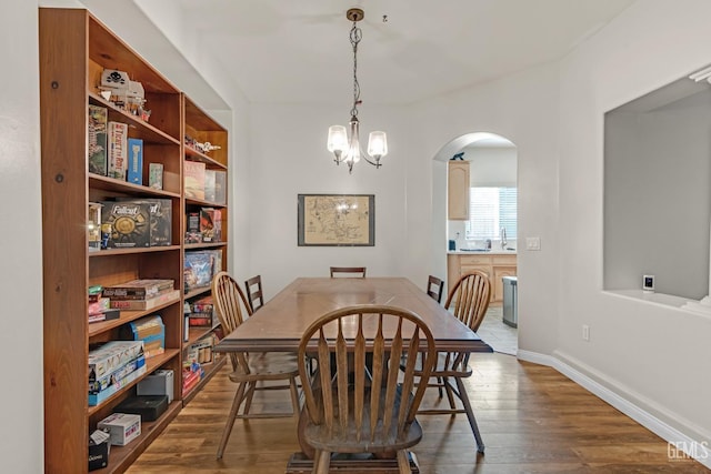 dining area with baseboards, arched walkways, dark wood finished floors, and a chandelier