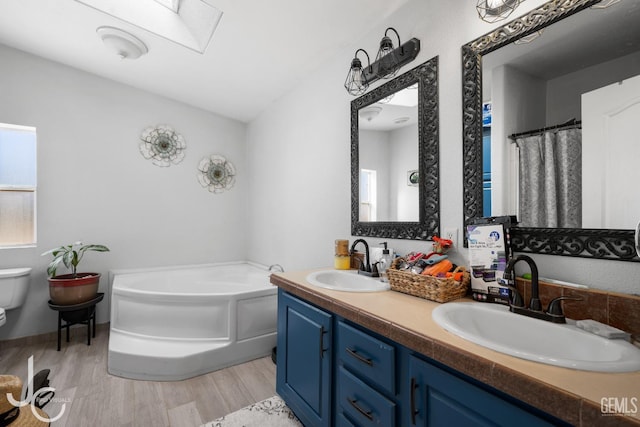 bathroom with vanity, a skylight, hardwood / wood-style flooring, toilet, and a tub to relax in