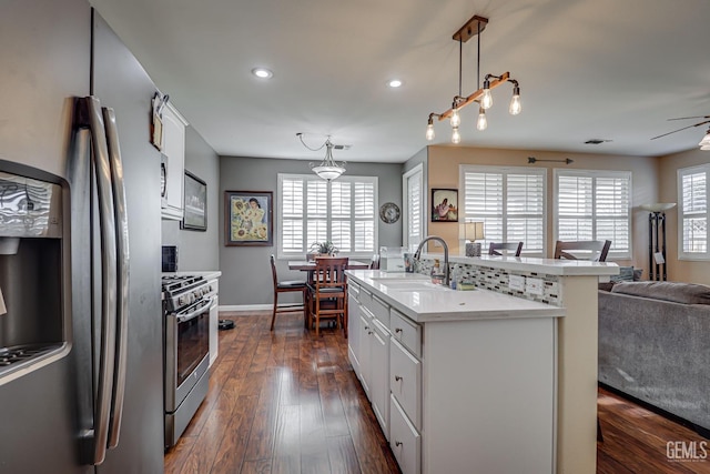 kitchen featuring pendant lighting, sink, appliances with stainless steel finishes, white cabinets, and a center island with sink