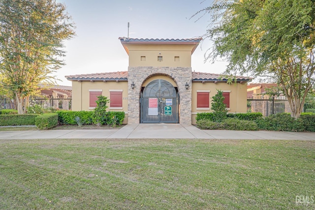 mediterranean / spanish home featuring stone siding, a front lawn, fence, and stucco siding