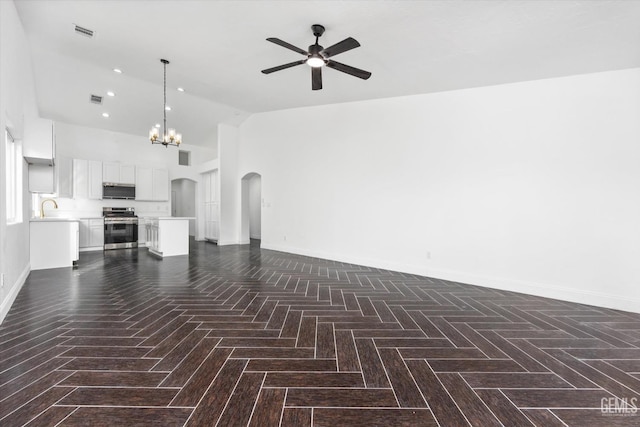 unfurnished living room featuring sink, dark parquet flooring, ceiling fan with notable chandelier, and high vaulted ceiling