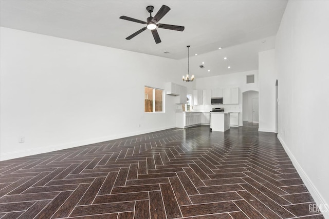 unfurnished living room featuring ceiling fan with notable chandelier, dark parquet floors, and high vaulted ceiling