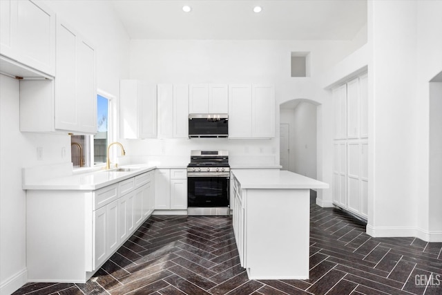 kitchen featuring sink, white cabinets, a high ceiling, kitchen peninsula, and stainless steel gas range oven