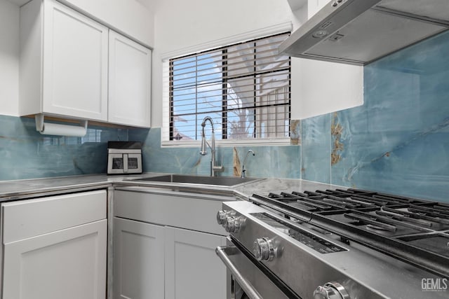 kitchen with under cabinet range hood, a sink, white cabinetry, stainless steel counters, and stainless steel gas stove