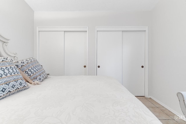 bedroom with baseboards, multiple closets, and light tile patterned flooring